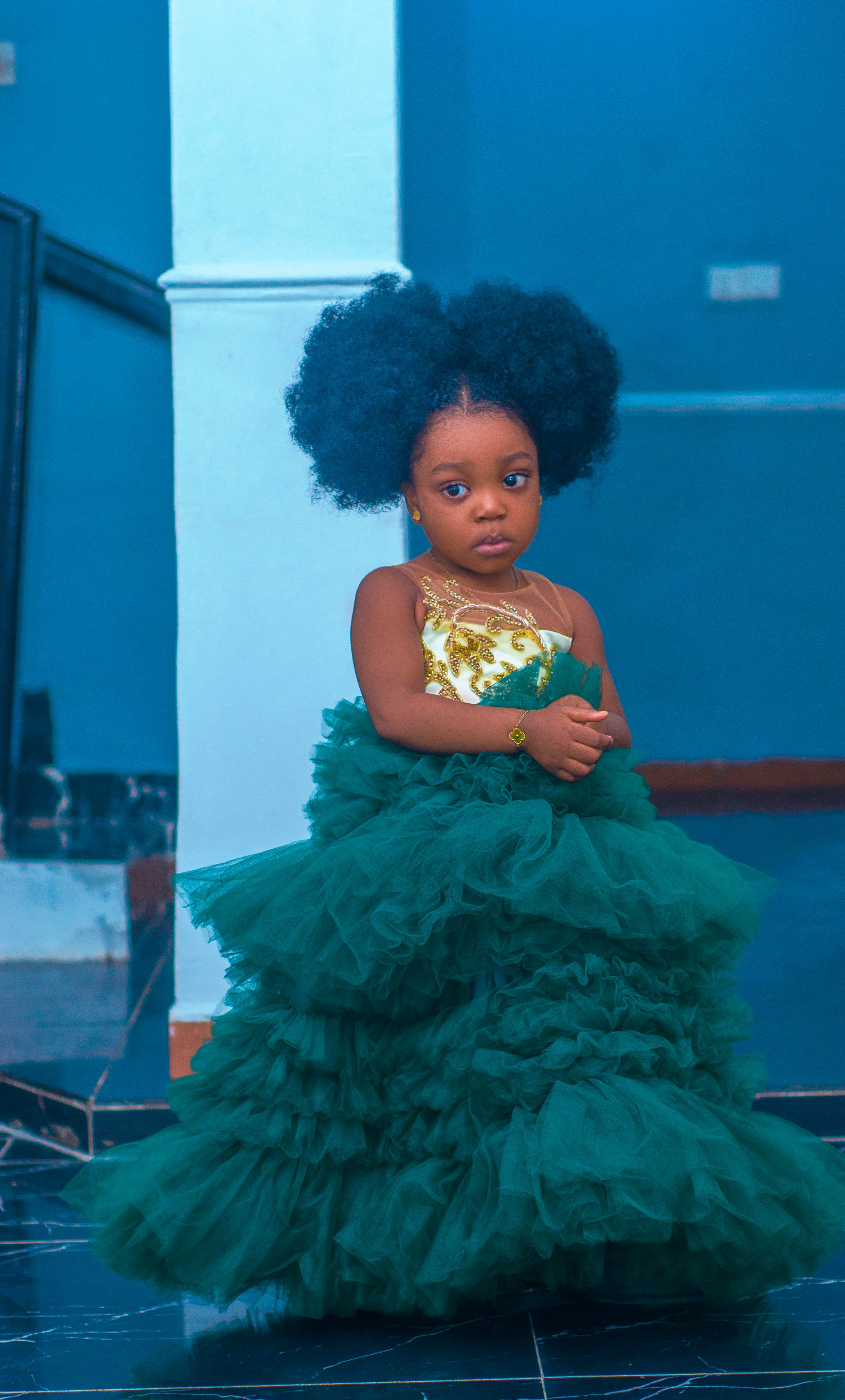 Charming young girl in a luxurious green gown posing indoors.