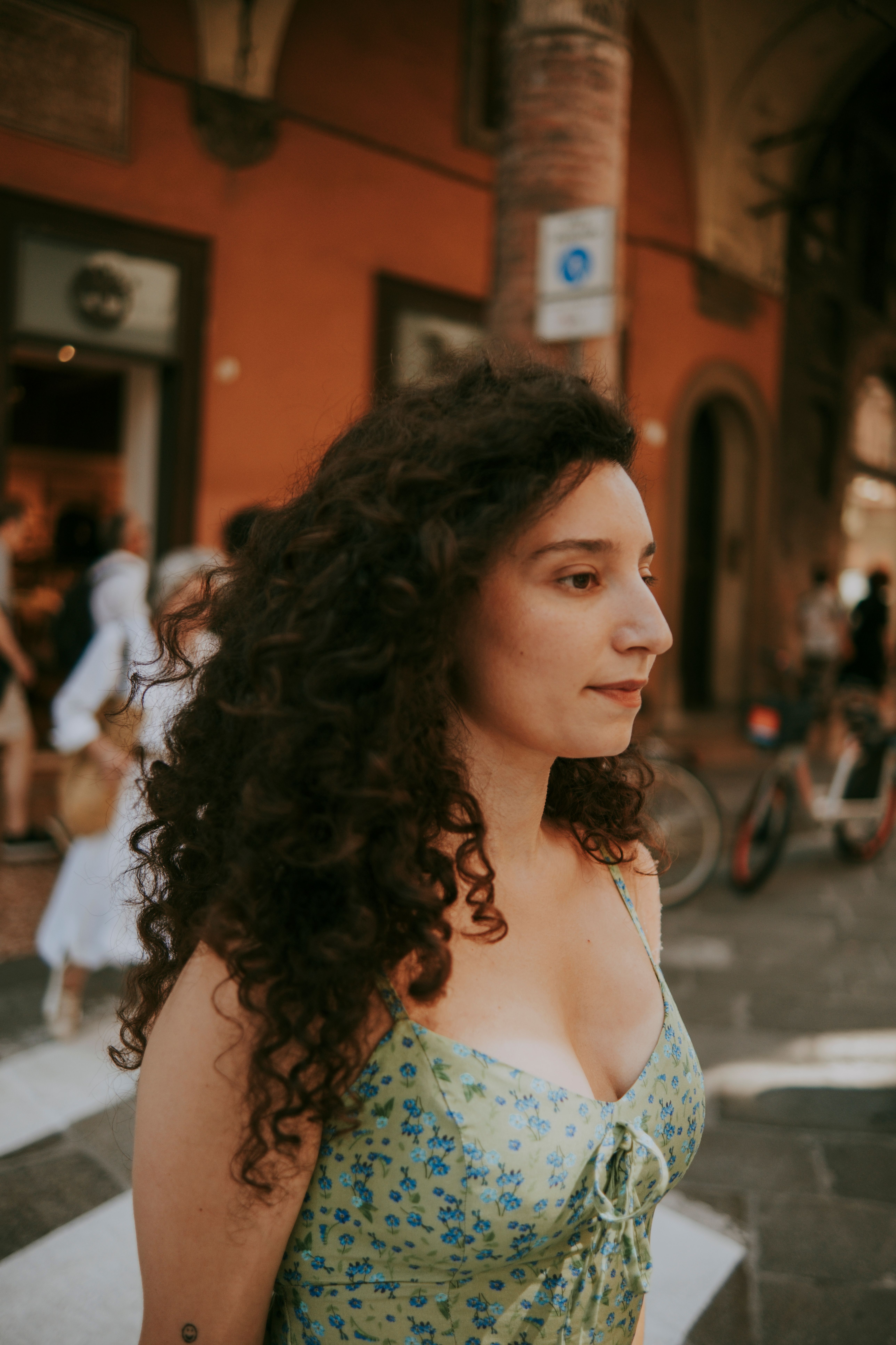 Stylish woman walks city street in floral sundress and curls. Urban chic.