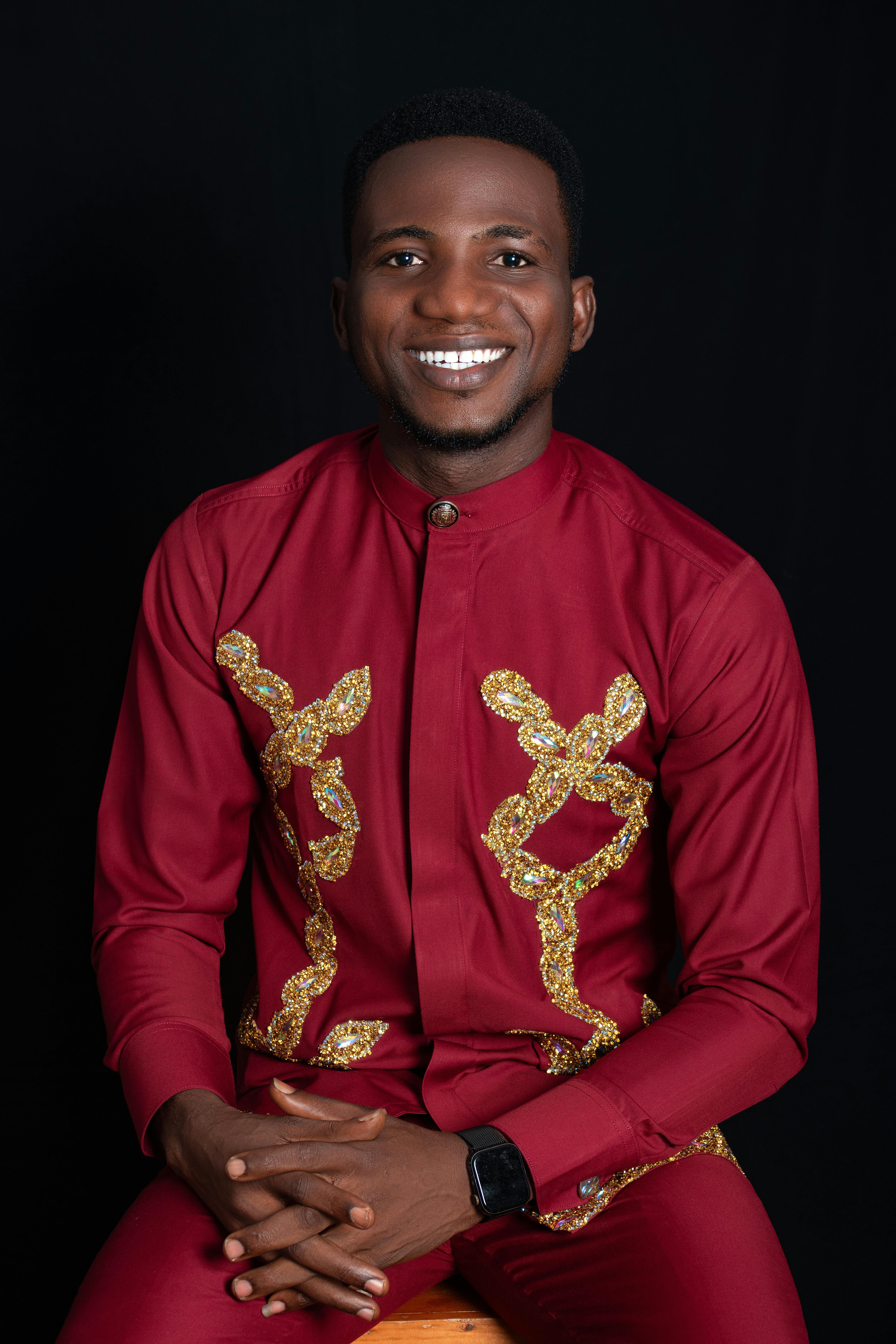 Portrait of a man in traditional red clothing with golden embroidery, smiling confidently.