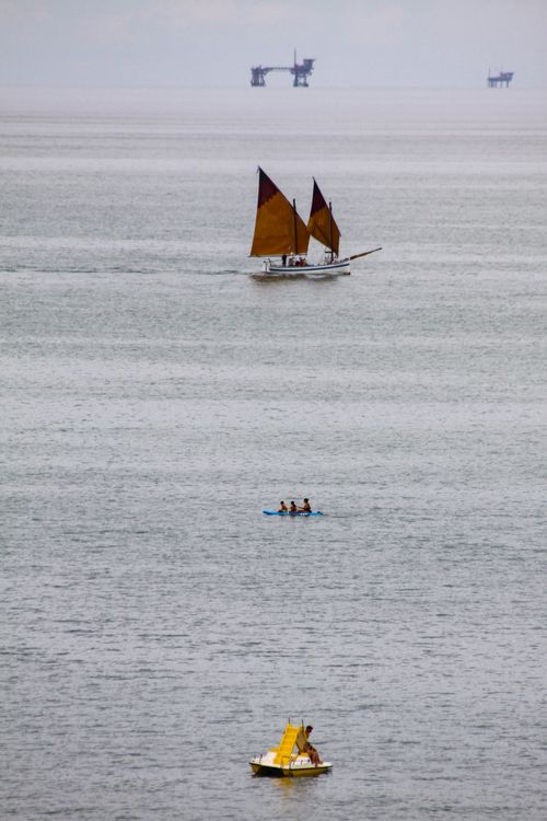Free A tranquil sea view featuring a sailboat, kayak, and distant oil platforms, captured on a clear day. Stock Photo