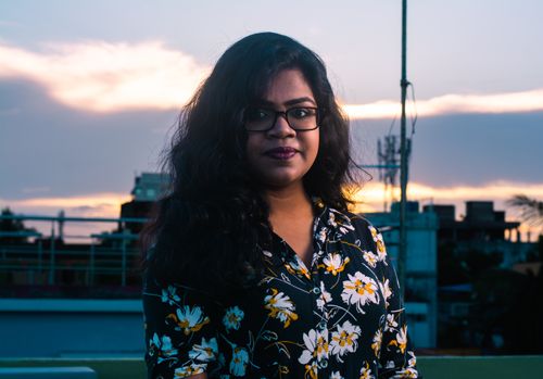 Free A woman with glasses in a floral shirt poses outdoors at twilight. Stock Photo