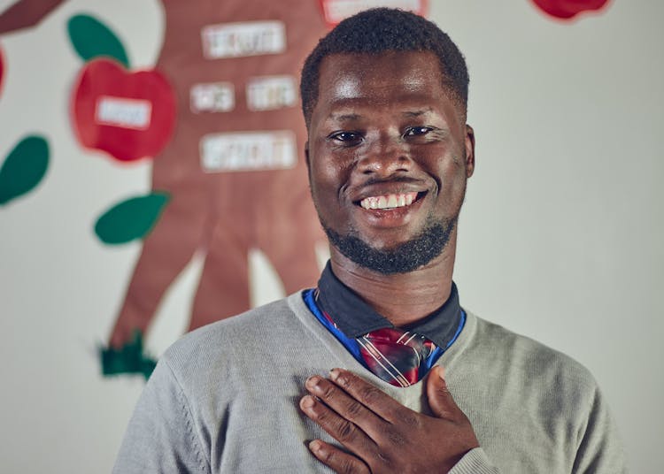 Young Man In A Sweater Smiling And Holding His Hand On His Chest 