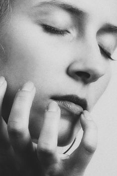 Black and white close-up portrait of a woman with closed eyes, hand near chin.