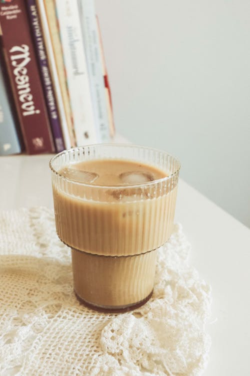 A glass of iced coffee sits on a table next to books