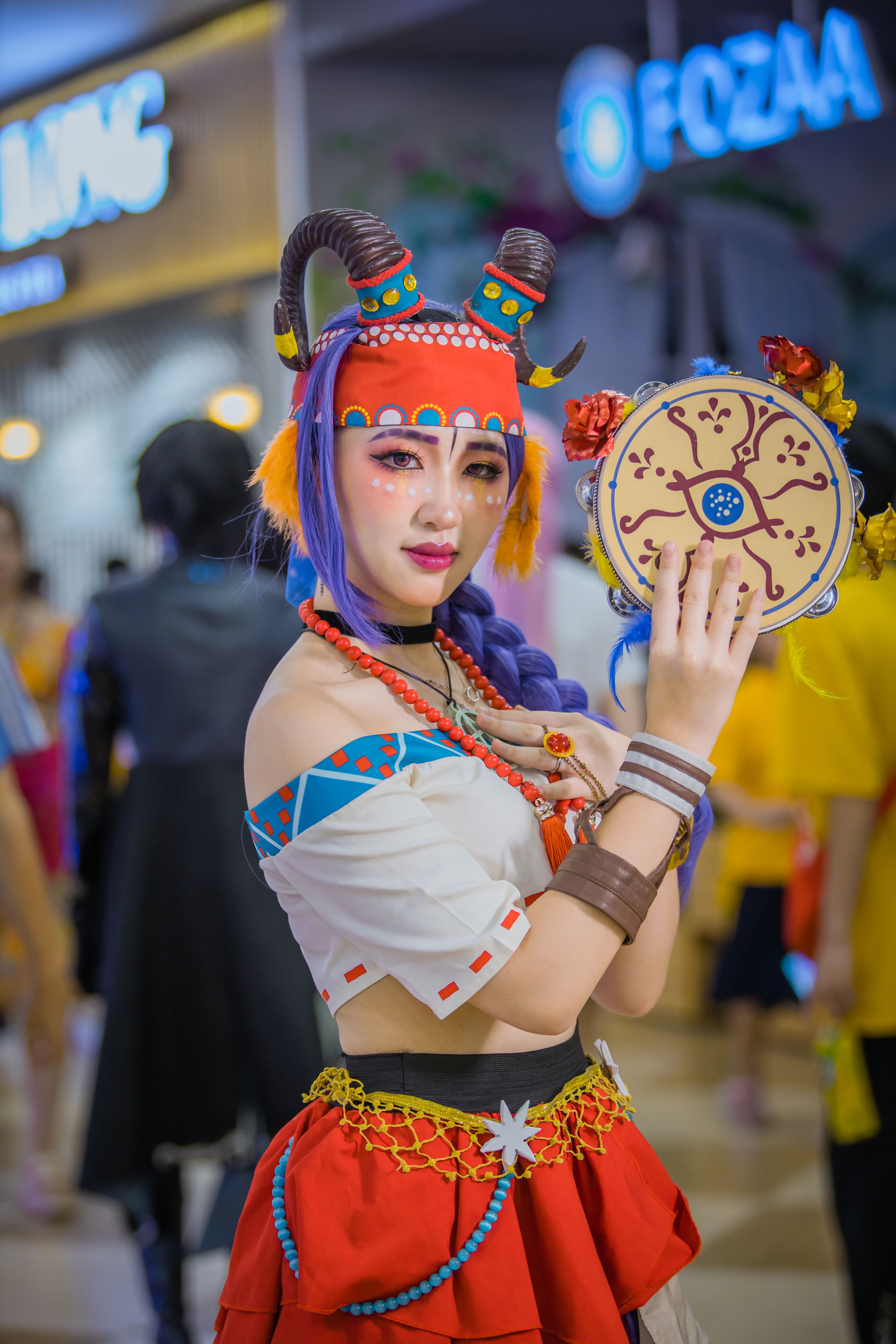 Colorful cosplay featuring a woman in a horned costume with bold accessories, set indoors.
