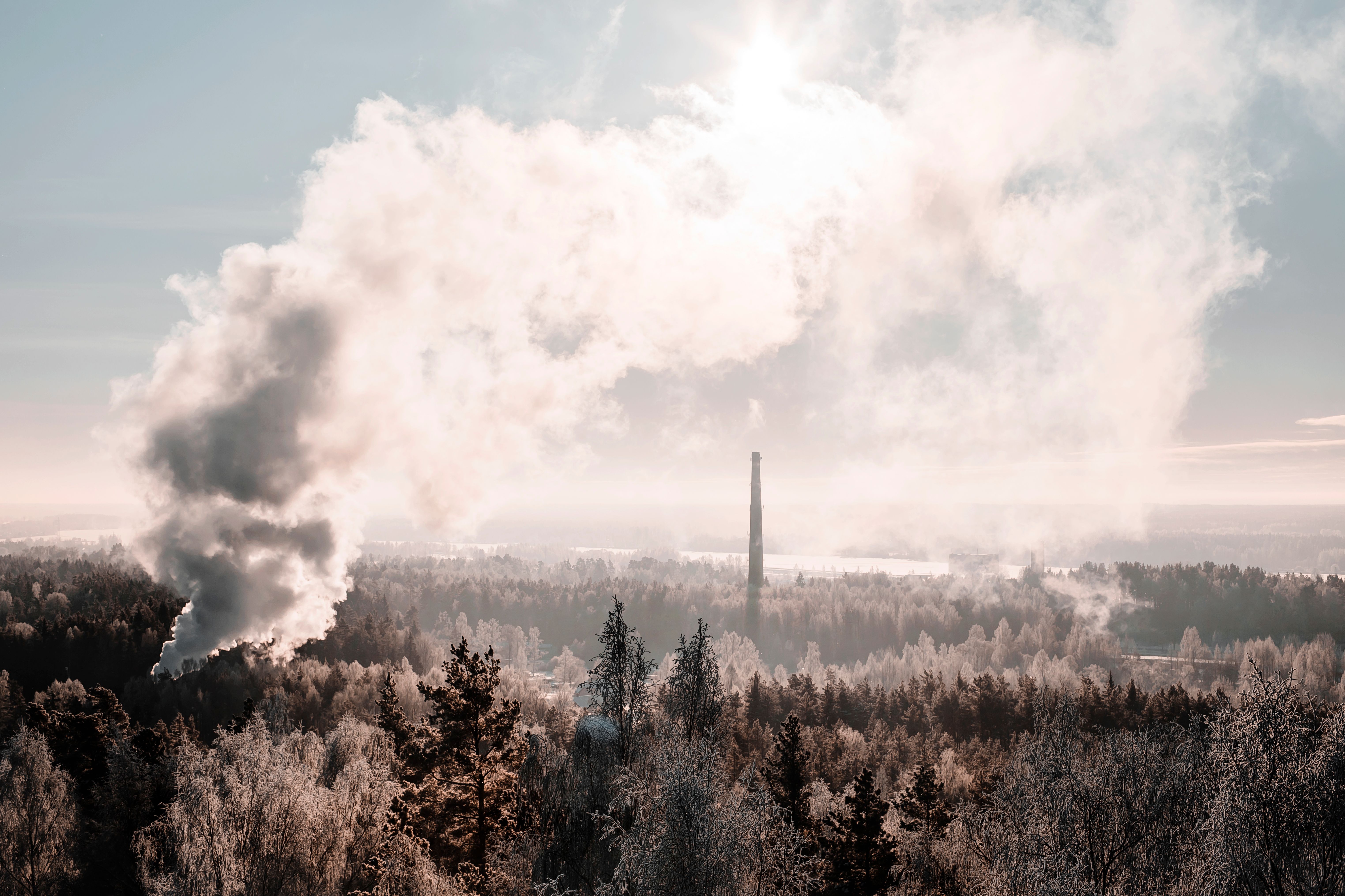 Aerial shot of a winter forest landscape with smoke rising, suggesting industrial activity.