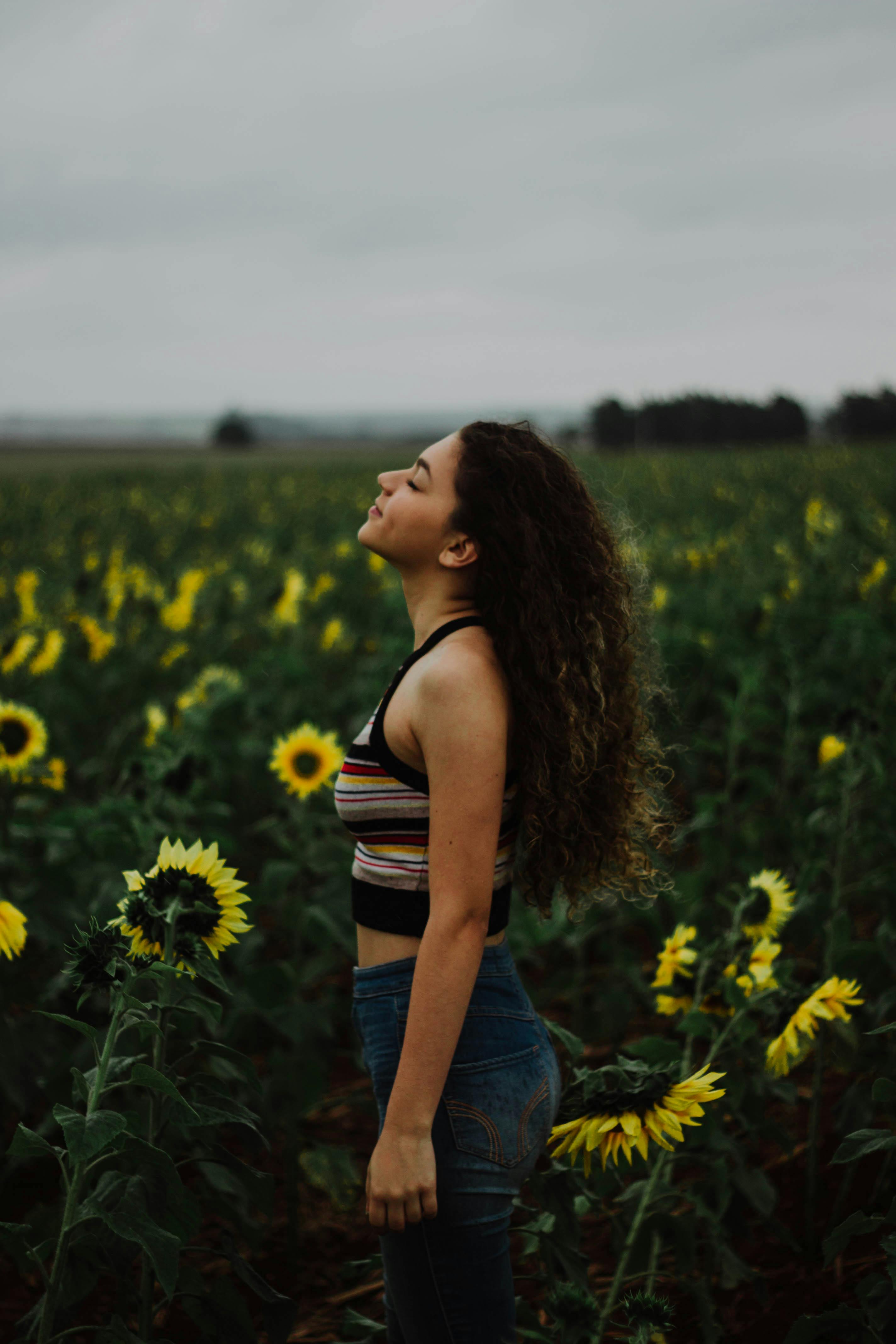 Young woman enjoying the tranquility of a sunflower field on a cloudy day.
