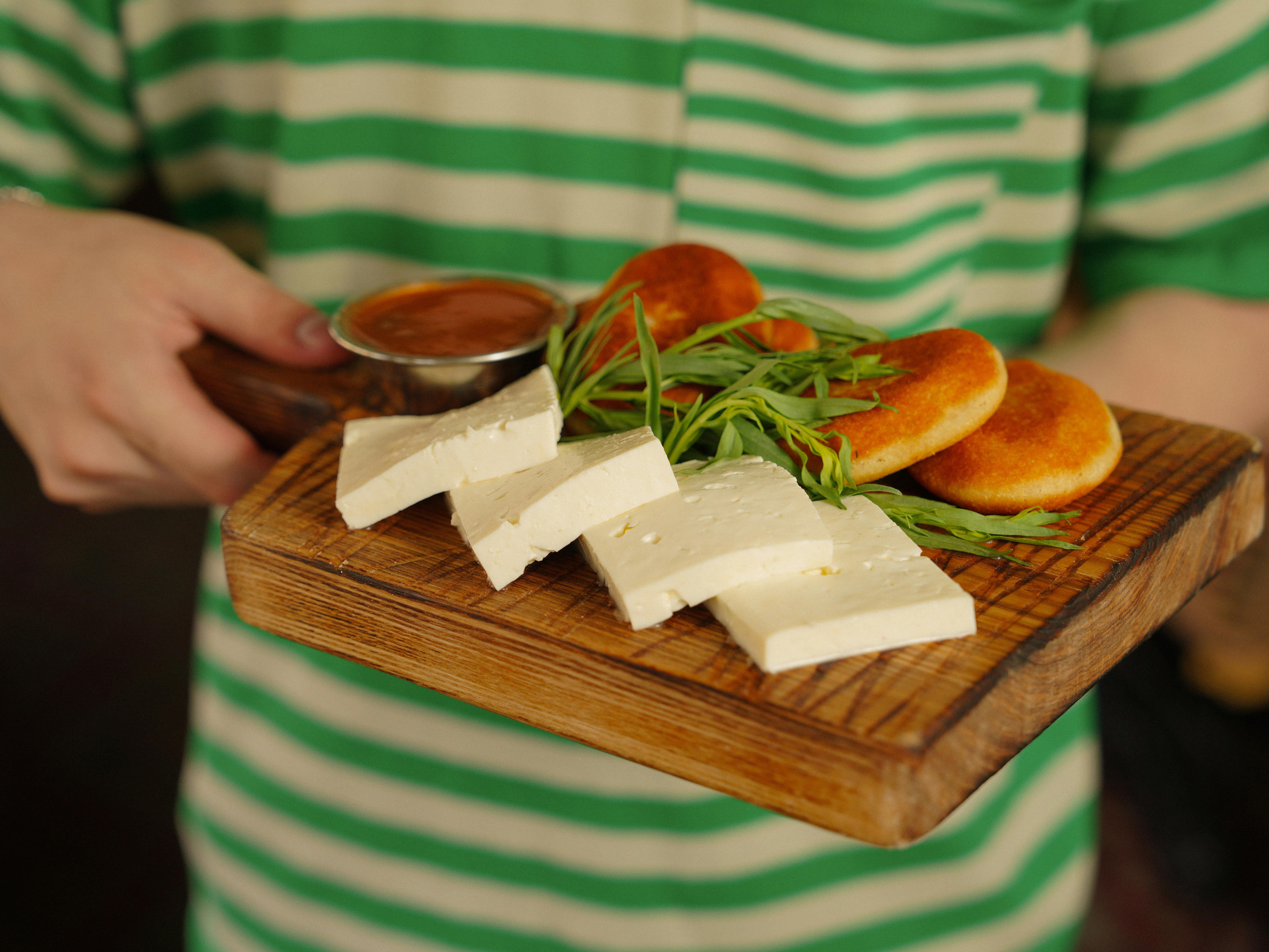 A close-up of cheese and pastries on a wooden tray with fresh greens and sauce.