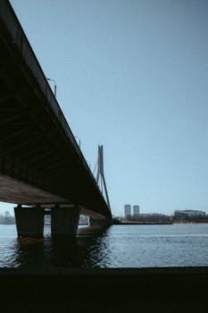Majestic urban bridge spanning a tranquil river under a clear blue sky.