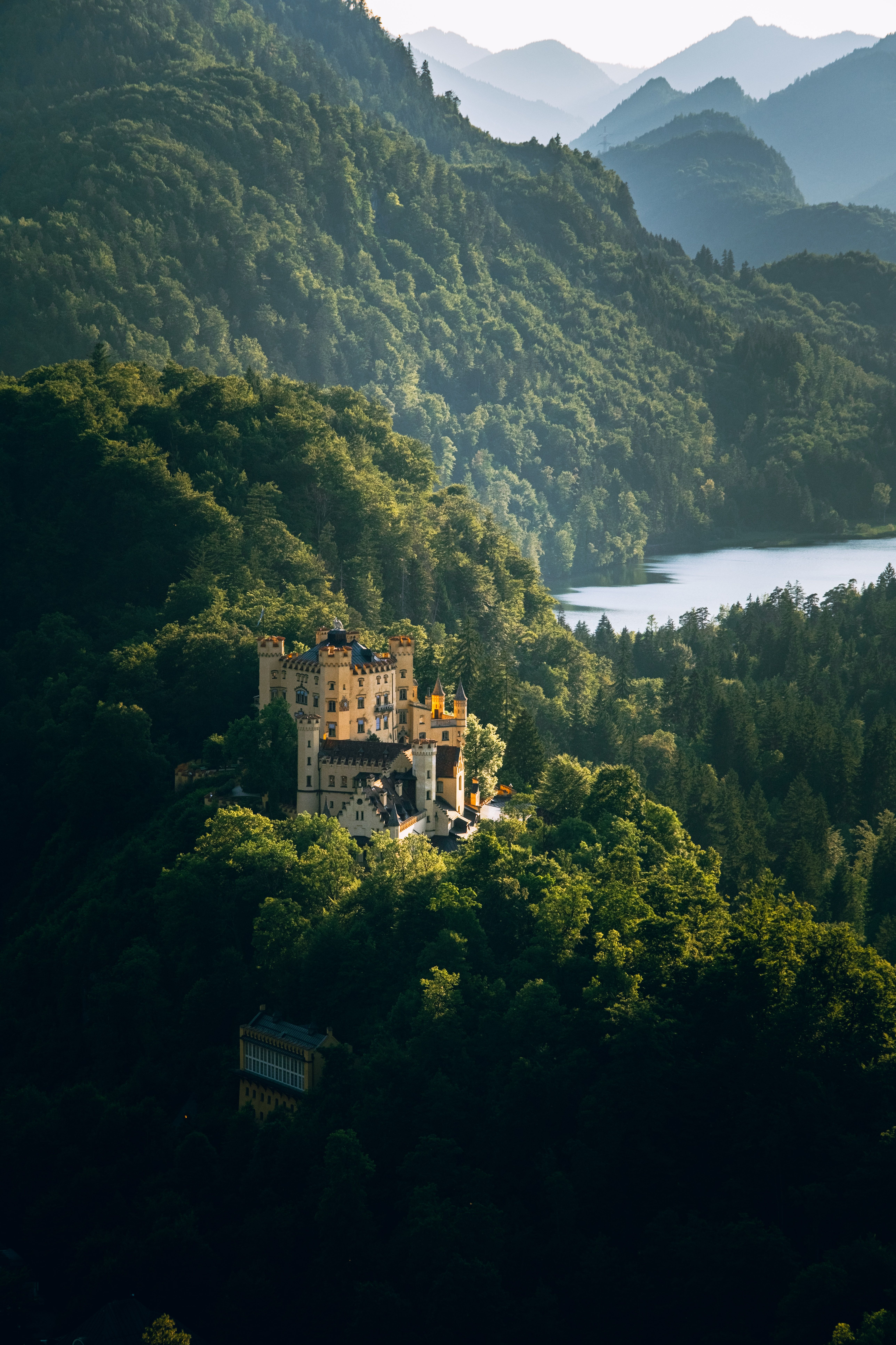 A castle sits on top of a mountain surrounded by trees · Free Stock Photo