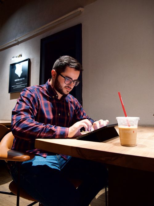 Free Young man focused on tablet at cafe table with iced coffee, creating an ambience of productivity. Stock Photo