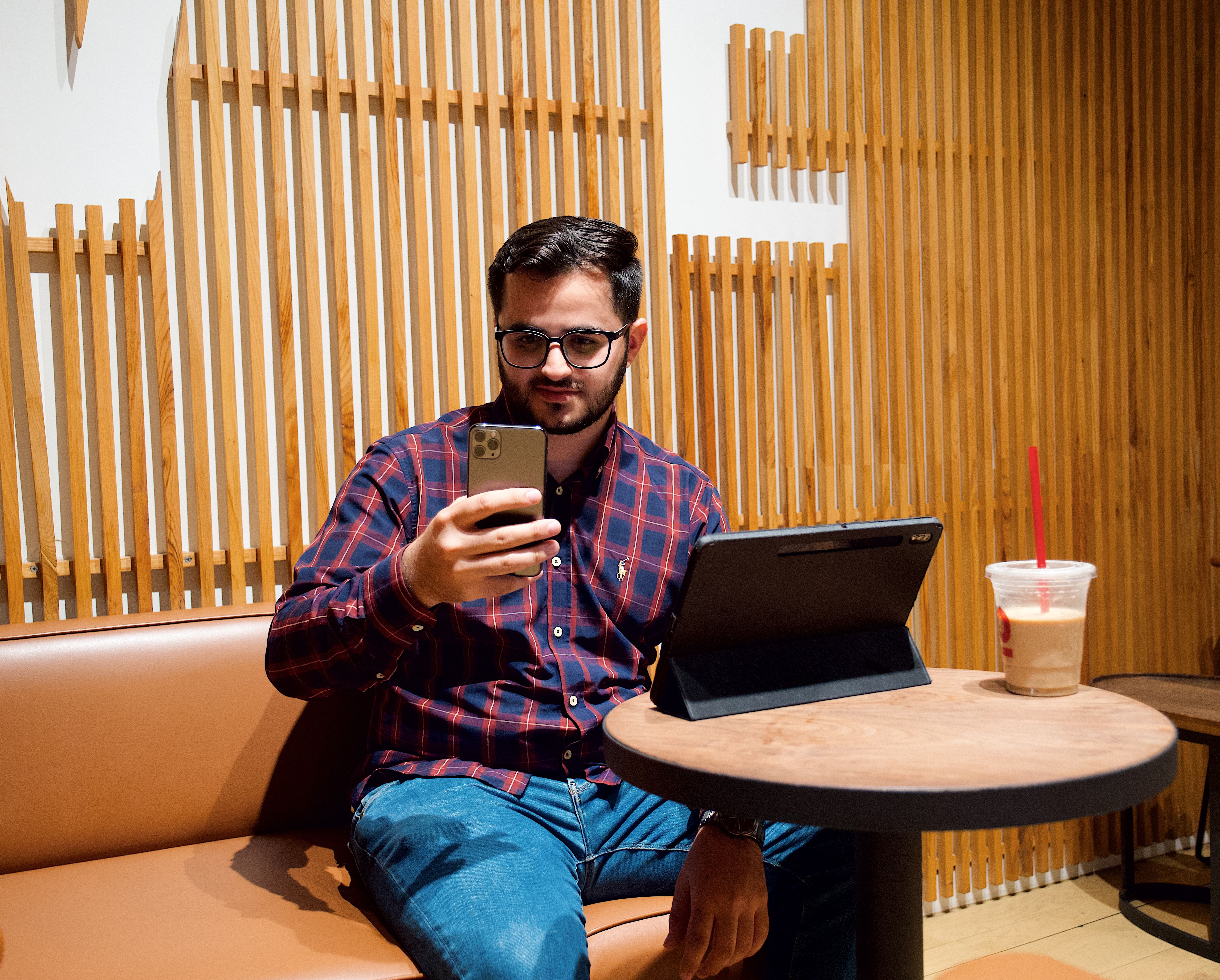 A young person holding a smartphone with a Bible app open, sitting in a coffee shop