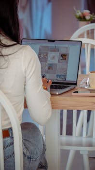 Woman seated at a table, using a laptop indoors with a warm atmosphere.