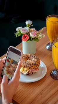 A person photographs a sesame seed bagel with orange juice in a cozy café.
