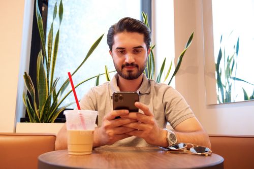 Free Young man checks phone in a stylish cafe with plants and iced drink. Stock Photo