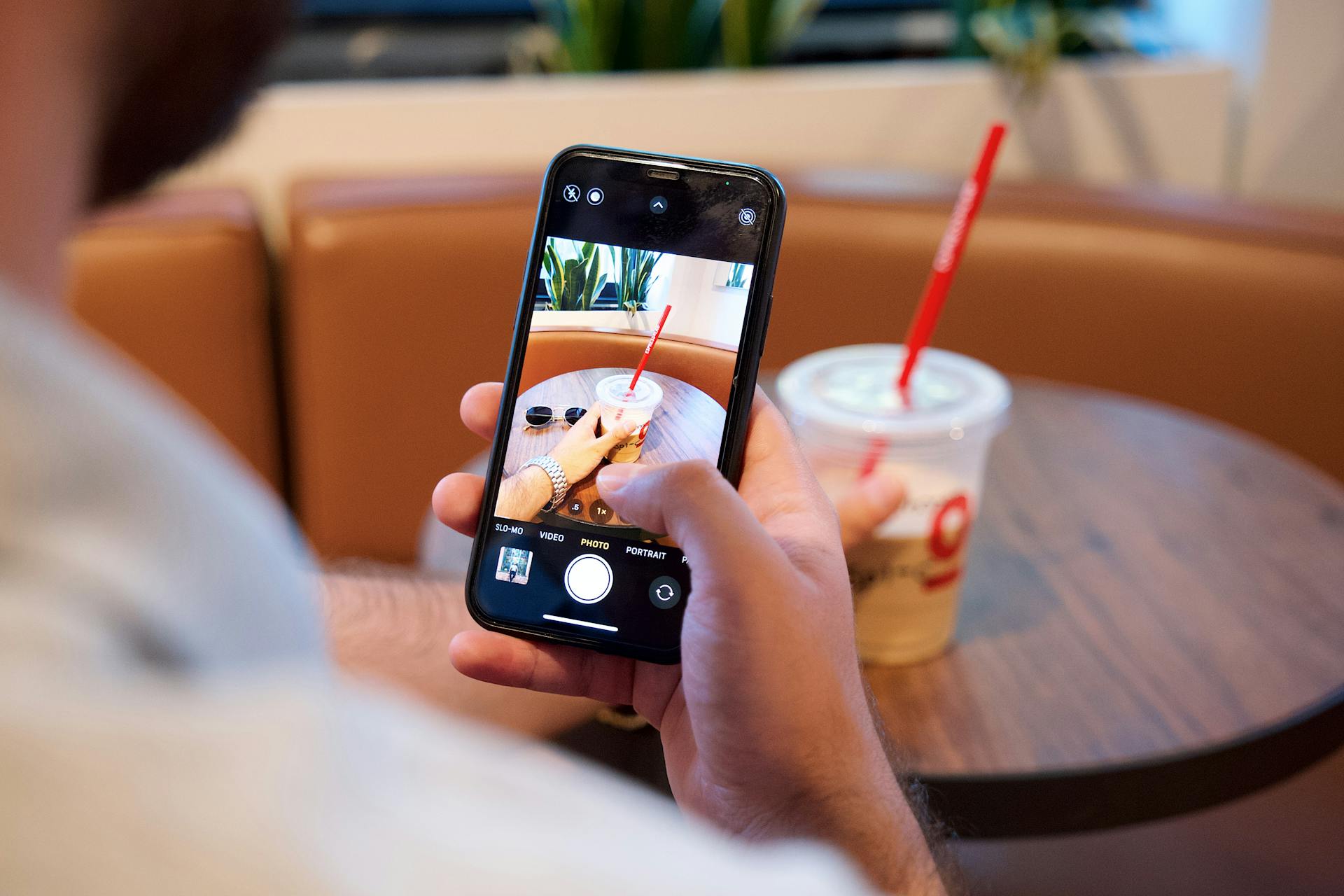 Man using smartphone to photograph a drink in a café with a disposable cup.