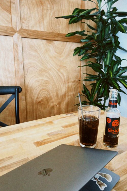 Free A cozy coffee shop corner in Dortmund, featuring a laptop, soda bottle, glass, and green plant. Stock Photo