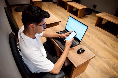 Man Sitting at a Desk with a Laptop and Using his Phone 