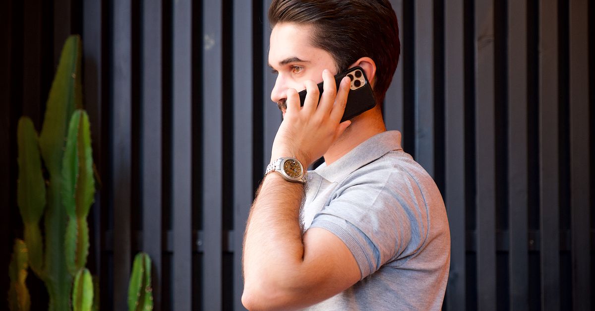 Um jovem em uma camisa casual se comunica em um smartphone enquanto usa um relógio de pulso.