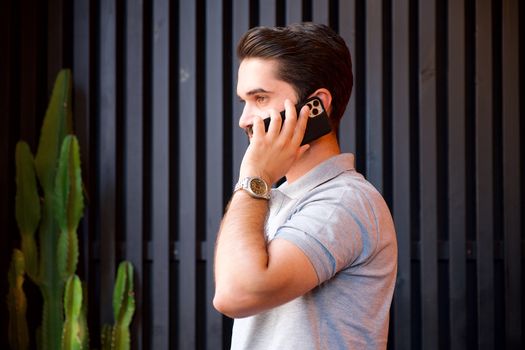 A young man in a casual shirt communicates on a smartphone while wearing a wristwatch.