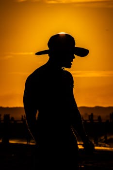 Dramatic silhouette of a man with hat against a vibrant sunset sky on a beach.