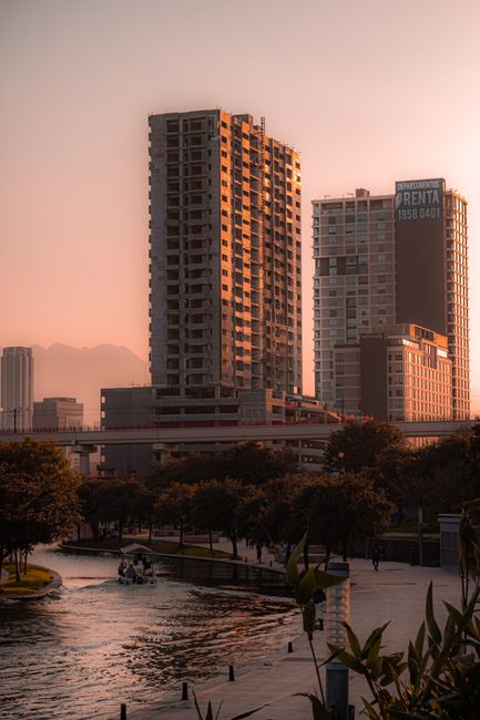 Dramatic sunset over Monterrey skyline with skyscrapers reflecting warm hues along the waterway.