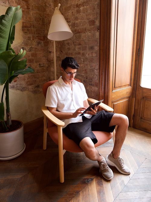 Free Man in white shirt using a tablet while seated in a cozy armchair indoors. Stock Photo
