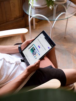 A man holding a tablet indoors, sitting comfortably in a bright living room.