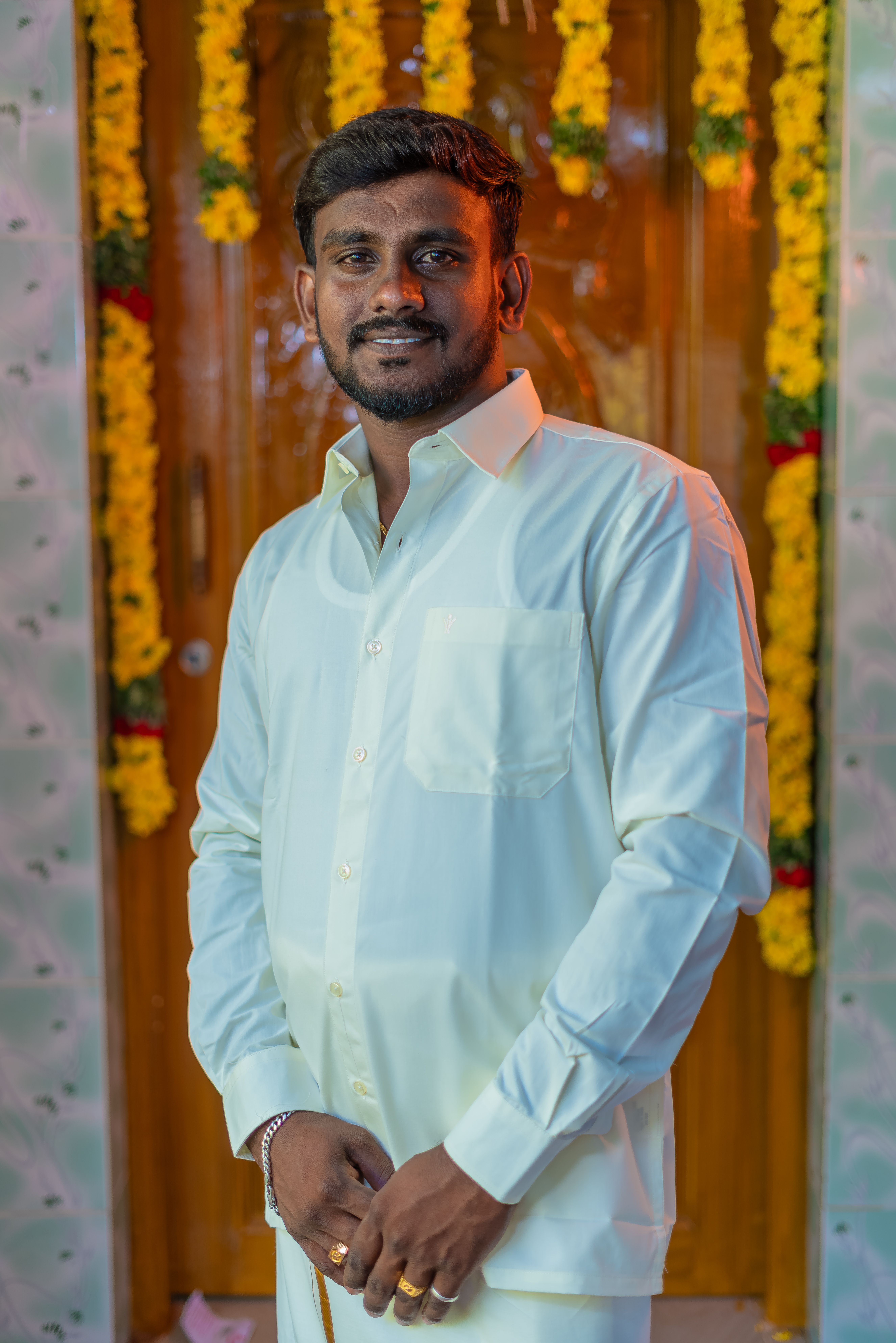 A man in a white shirt smiling indoors with floral decorations.