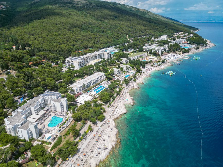 Discover Rabac's coastline with turquoise waters and resort-lined shores from an aerial perspective.
