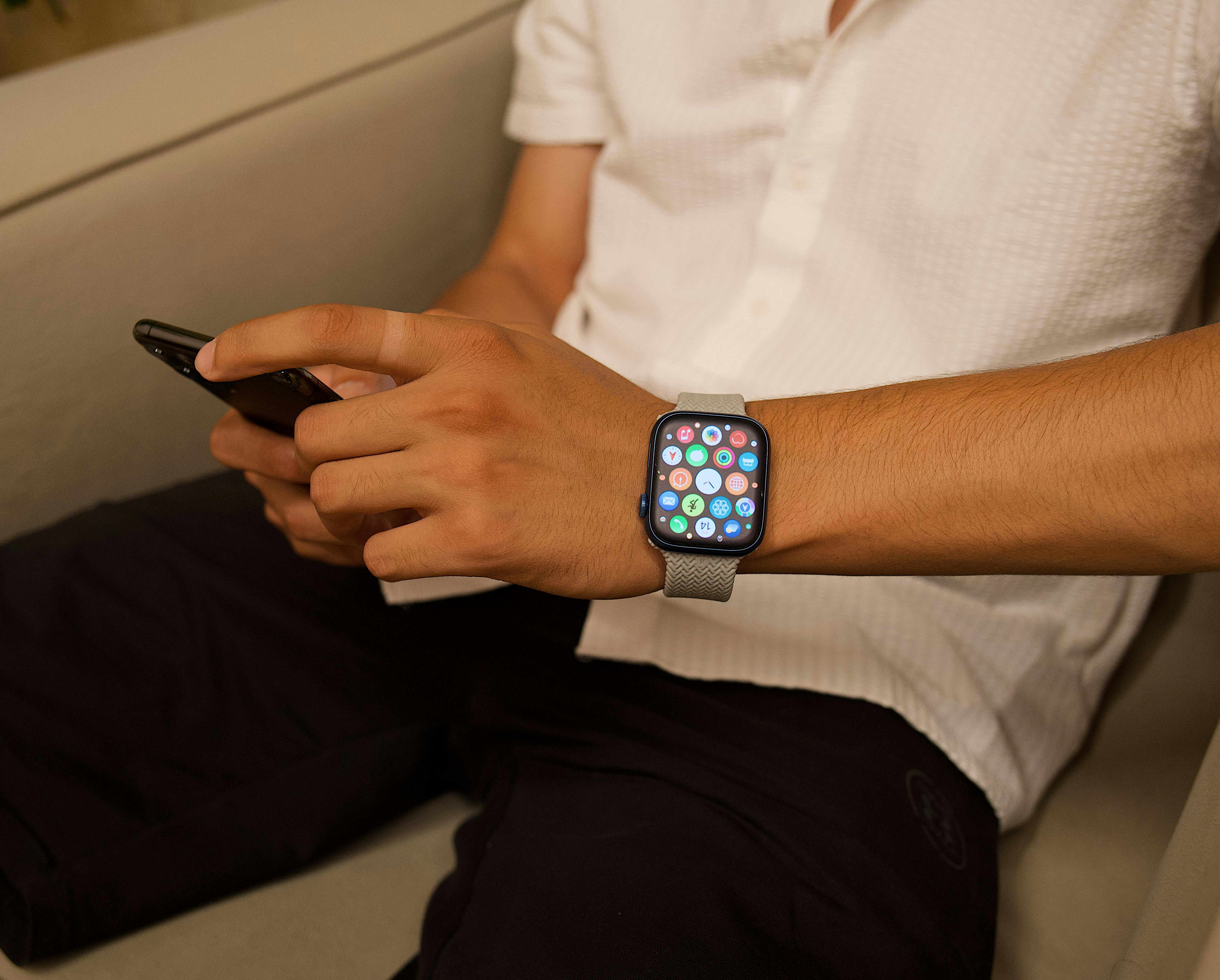 A person sitting indoors, interacting with a smartphone and smartwatch.