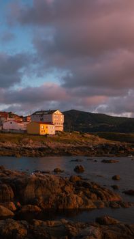 A picturesque view of a coastal village with rocky shores under a dramatic evening sky.