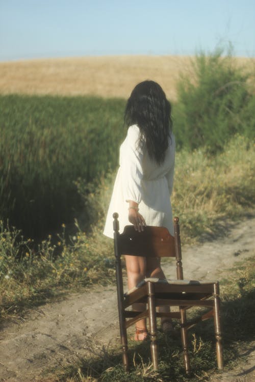 Woman Standing with Chair on Dirt Road on Field
