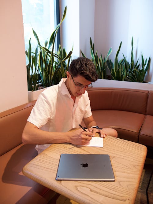 Man in Shirt Sitting by Table with Laptop