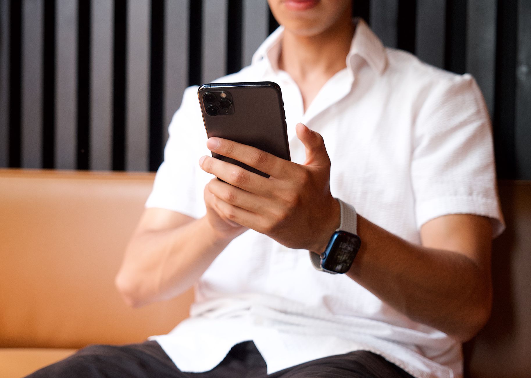 Close-up of a man in a white shirt using a smartphone and smartwatch indoors.
