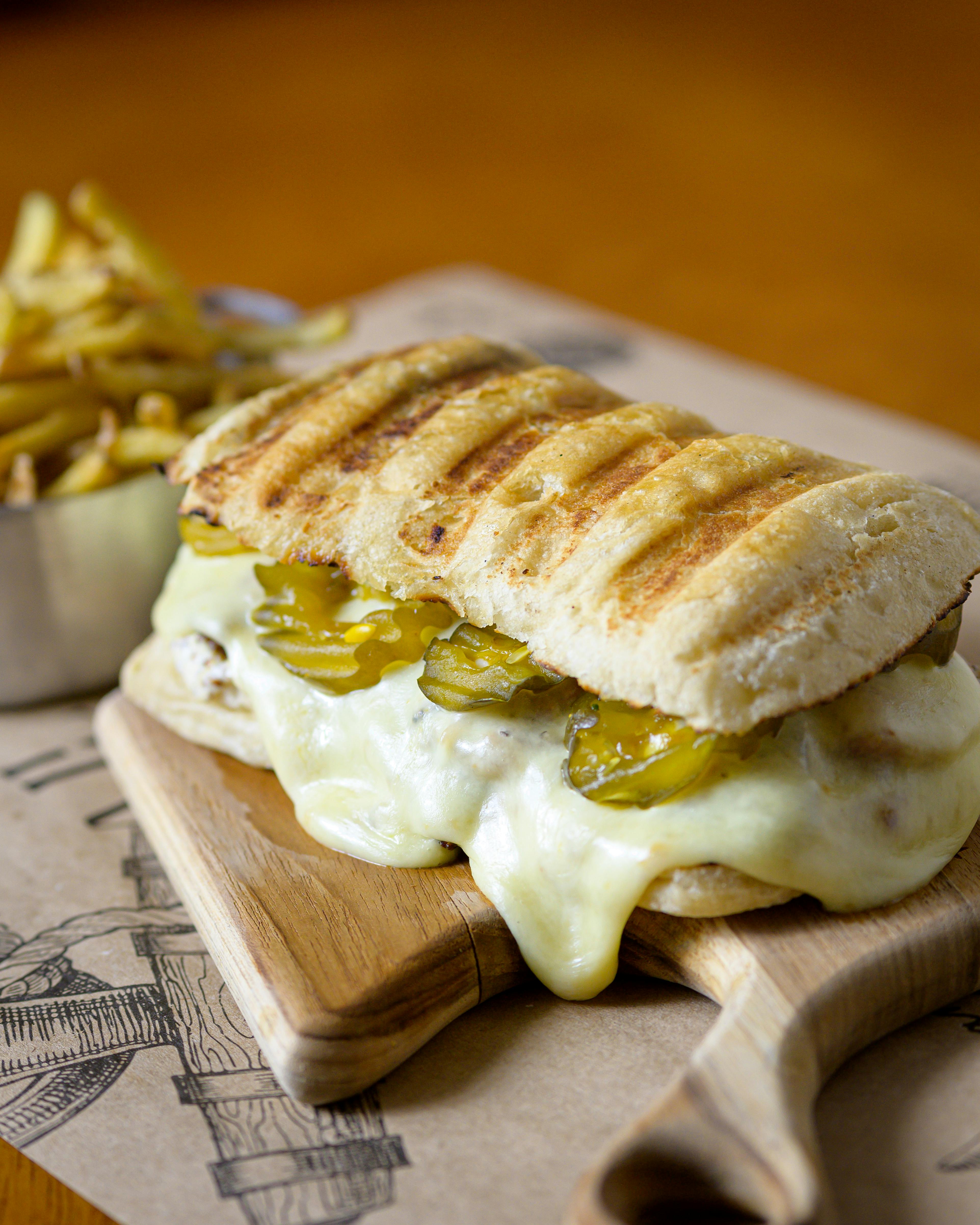 Close-up of a grilled cheese and pickle sandwich served with fries on a wooden tray.