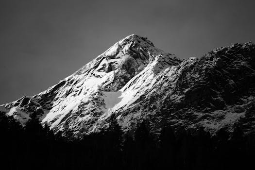 A dramatic black and white photograph of a snow-capped mountain peak, evoking a sense of adventure and tranquility.
