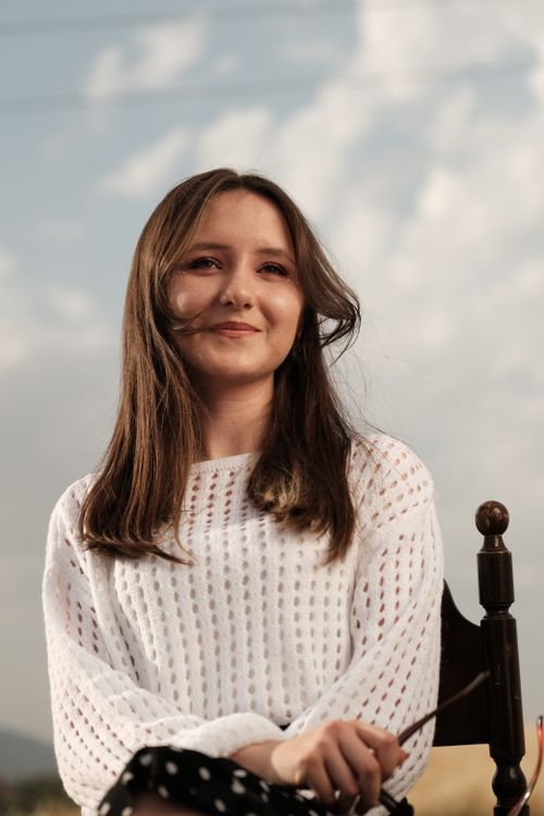 Free A serene portrait of a woman sitting on a chair outdoors in natural light wearing a white knitted blouse. Stock Photo