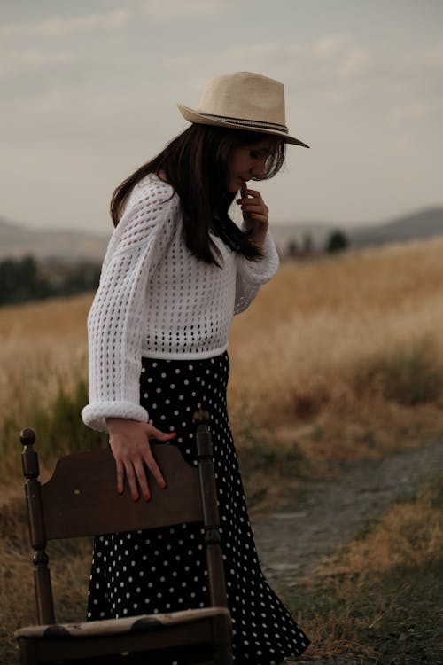 Model in a white sweater and hat looking down at her feet on a dirt road