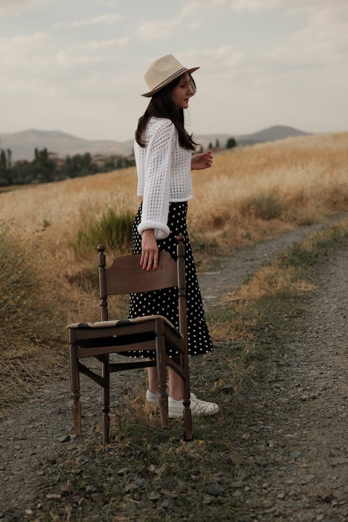 Model Holding a Chair on a Dirt Road through the Fields