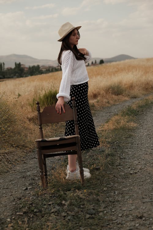 Model in a White Sweater and a Black Polka Dot Midi Skirt on a Dirt Road Among the Fields