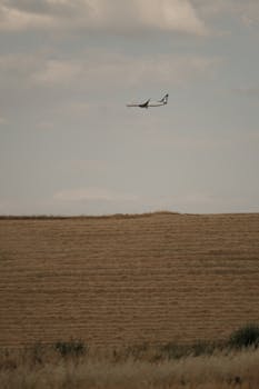 A sleek airplane flying above a serene rural field, showcasing harmony between technology and nature.