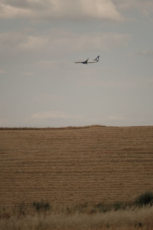 Free A sleek airplane flying above a serene rural field, showcasing harmony between technology and nature. Stock Photo
