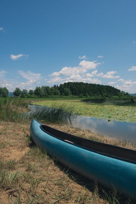 A tranquil scene with a blue canoe by a riverbank under a clear summer sky.