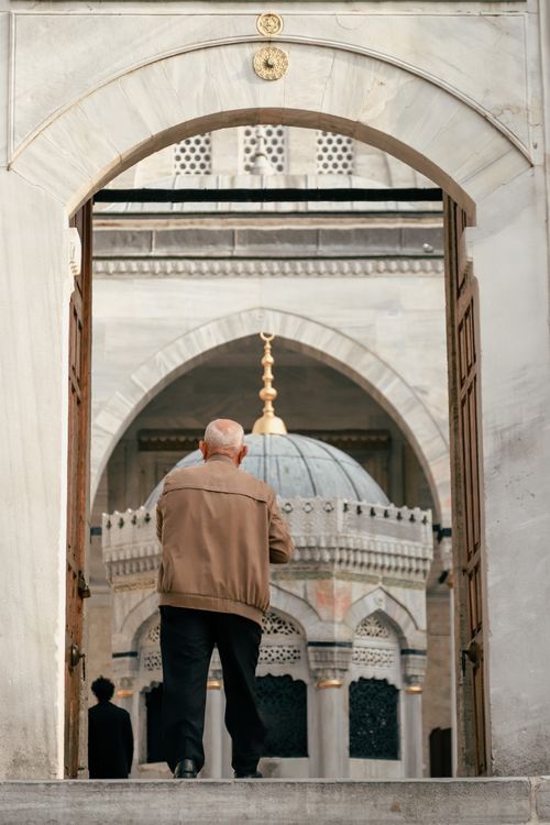 Free Elderly man standing at mosque entrance, capturing religious architectural beauty in the city. Stock Photo