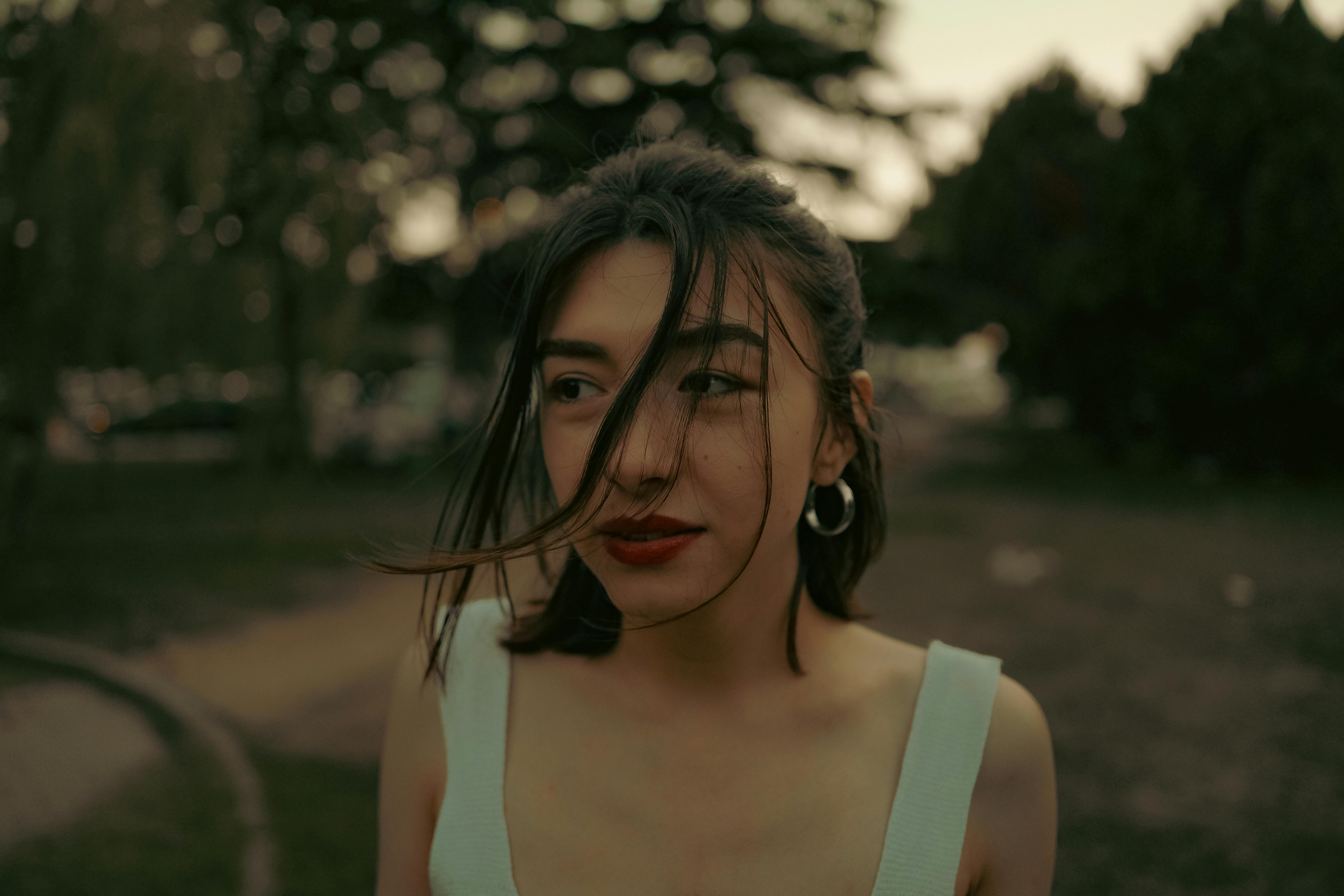 Serene portrait of a woman outdoors with windblown hair and soft background.
