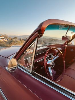 Close-up of a vintage red cabriolet car interior with scenic sunset view.