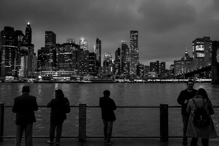 Silhouette Of People Standing On Brooklyn Bridge And Looking At A Cityscape Of New York 