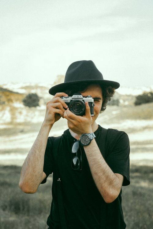 Free A young man with a camera in a black hat taking photos outdoors. Stock Photo