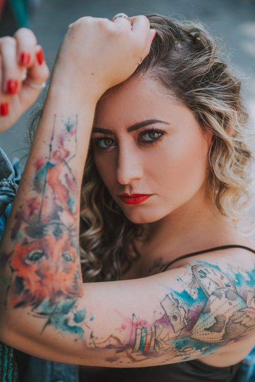 Free Close-up portrait of a woman showing colorful arm tattoos, with focus on expression and art. Stock Photo